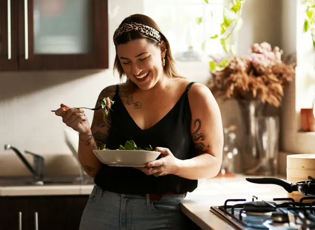 Woman, diet and person eating salad in her home kitchen and is happy for a meal with nutrition or healthy lunch. Smile, food and young female vegan in her apartment or house and eat vegetables