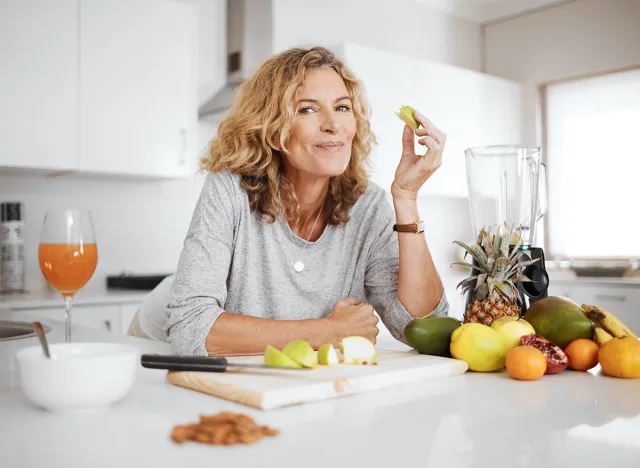 Portrait, fruit salad and apple with a senior woman in the kitchen of her home for health, diet or nutrition. Smile, food and cooking with a happy mature female pension eating healthy in the house