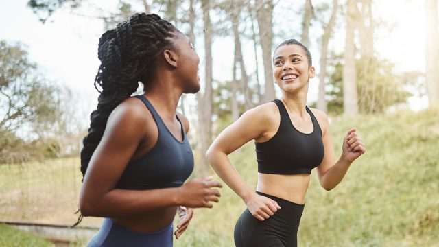 Happy woman, friends and running in forest for workout, training or outdoor cardio exercise together. Active female person, athlete or runners smile for sports run, sprint or race in nature fitness