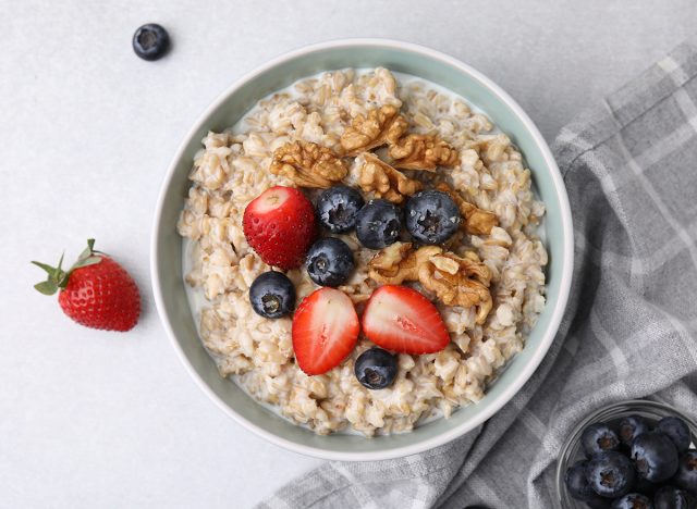 Tasty oatmeal with strawberries, blueberries and walnuts in bowl on grey table, flat lay