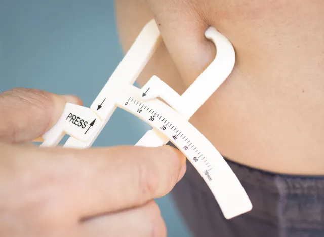 Slim attractive young man using fat caliper to measure bodyfat on waist line.