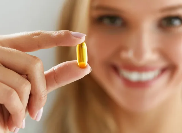 Healthy Diet Nutrition. Beautiful Smiling Young Woman Holding Fish Oil Pill In Hand. Closeup Of Happy Girl Taking Capsule With Cod Liver Oil, Omega-3. Vitamin And Dietary Supplements. High Resolution