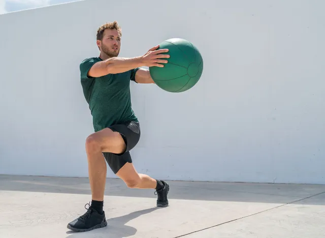 Working out man training legs and core ab workout doing lunge twist exercise with medicine ball weight. Gym athlete doing lunges and torso rotations for abs training.