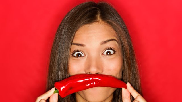 chili woman funny on red background holding red chili pepper vegetables as mustache looking funny at camera. Beautiful multicultural Caucasian / Chinese Asian girl on red background.