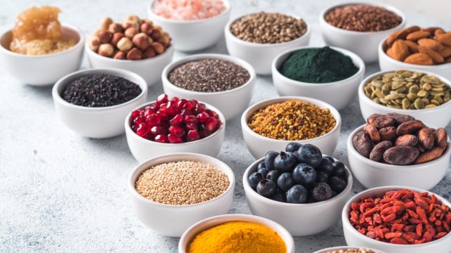 Various superfoods in smal bowl gray concrete background. Superfood as chia, spirulina, raw cocoa bean, goji, hemp, quinoa, bee pollen, black sesame, turmeric.