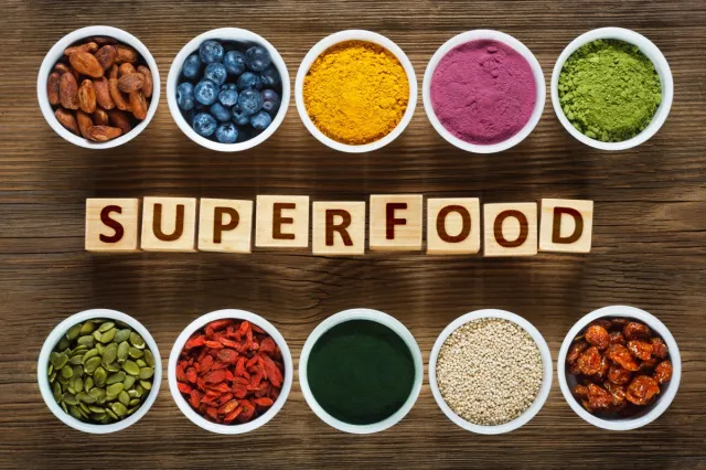 Superfoods as acai powder, turmeric, matcha green tea, spirulina, quinoa, pumpkin seeds, blueberry, dried goji berries, cape gooseberries (physalis peruviana), raw cocoa, hemp seeds on wooden table.