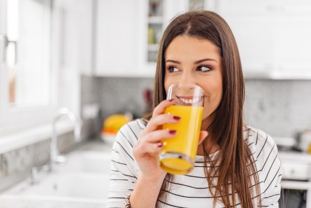 Close up of teenage woman drinking juice while looking through a window.