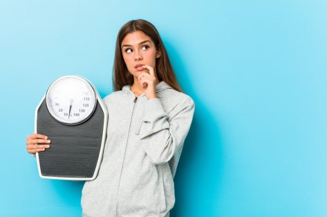 Young fitness woman holding a scale relaxed thinking.