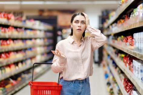 Portrait of young shocked caucasian woman holds cart and takes hand to head.