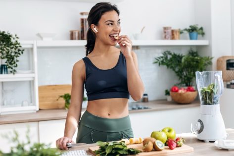 Shoot of athletic woman cutting fruits and vegetables to prepare a smoothie while listening to music with earphones in the kitchen at home.