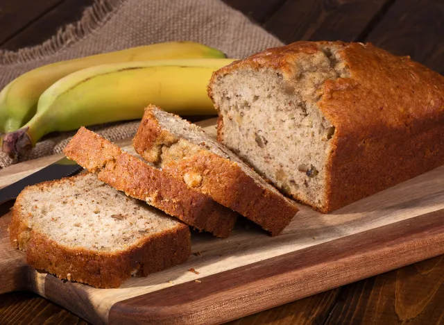 Banana nut sweet bread sliced on a wooden cutting board with bananas in background