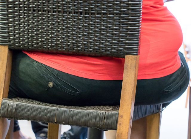 The back part of the fat body sitting on a chair. The detail of the obese person. A fat man sitting on chair in a restaurant.