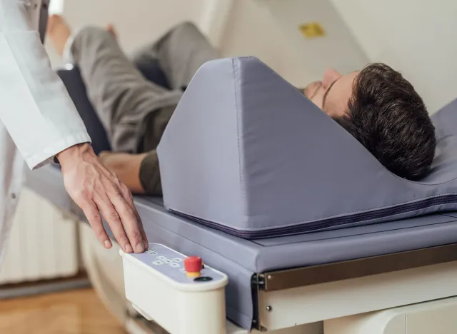 Hand of a medical technician operating the bone densitometer while his patient is lying on the bed.