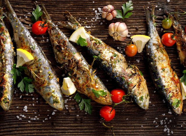 Grilled sardines with addition of fresh herbs, lemon and spices on a wooden background. Grilled seafood, barbecue