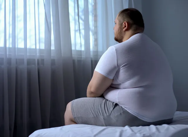 Sad heavy man sitting on bed at home, health problem, depression, insecurities