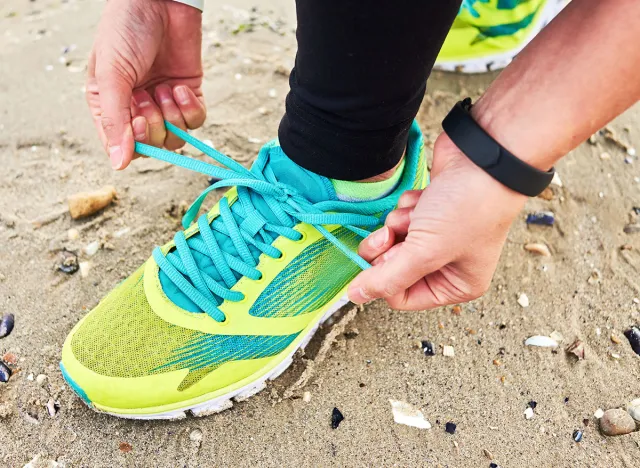 Woman tying running shoe laces preparing for run on ocean beach, copy space, closeup. Cropped image of female fitness runner getting ready for jogging outdoors