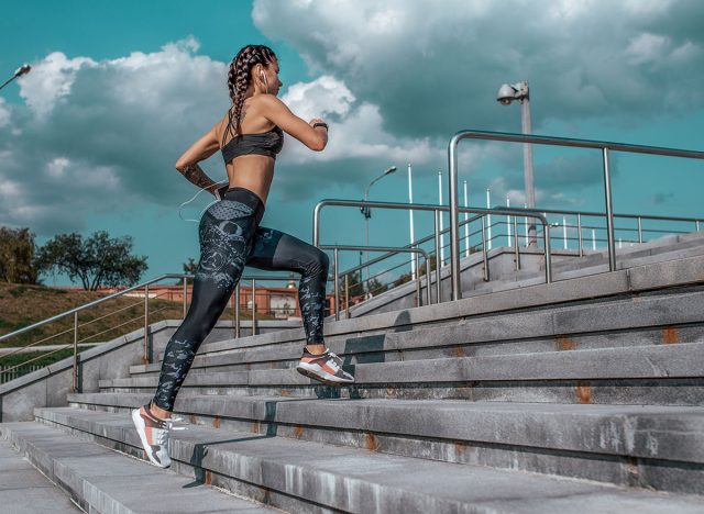 Girl runs in the summer in the city, on the morning run. Stair background, blue sky with clouds. Clothing leggings top. Free space for text. Phone earphones.