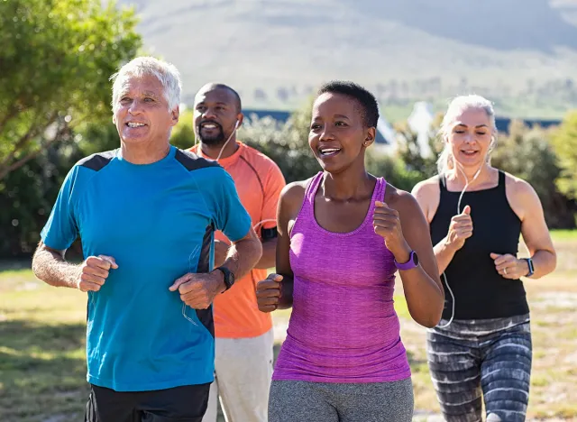 Healthy group of mature people jogging on track at park. Happy senior couple running at park with african friends. Multiethnic middle aged friends exercising together outdoor.