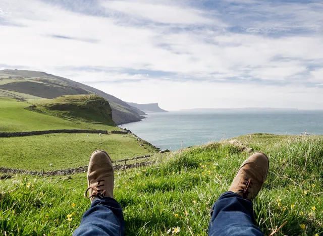 Man laying on the ground in a grass field, resting on a hill in the County Antrim, Northern Ireland