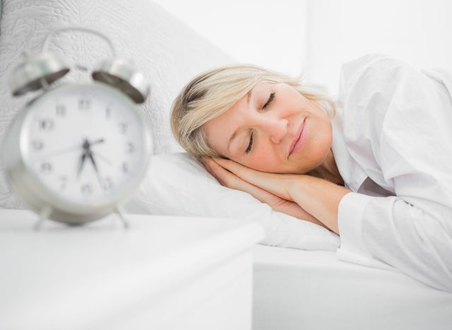 Woman sleeping in bed peacefully at home beside alarm clock