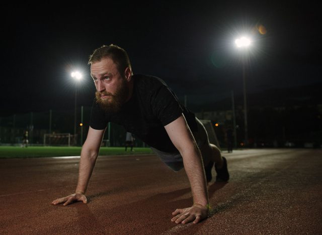 Young athletic bearded man doing push-ups muscular and strong guy exercising on night sport arena