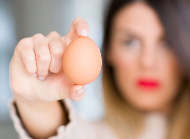 Young beautiful woman holding fresh egg at home with angry face, negative sign showing dislike with thumbs down, rejection concept