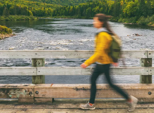 Hiker woman with backpack crossing river walking on bridge. Motion blur of tourist traveling in outdoor nature landscape fall autumn background panorama banner. Quebec, Canada.