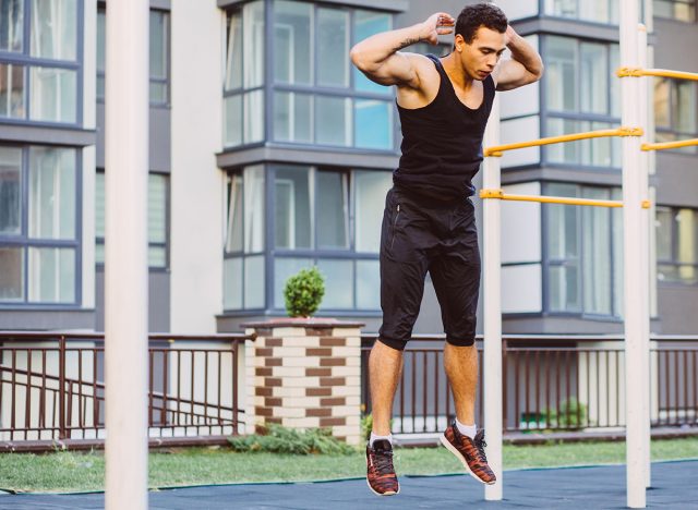 Jump up burpee. Sport exercises. Stage and release of squat. Exercises with free weight. Mixed race black man workout jump exercise on sport ground outdoor with urban cityscape on background.