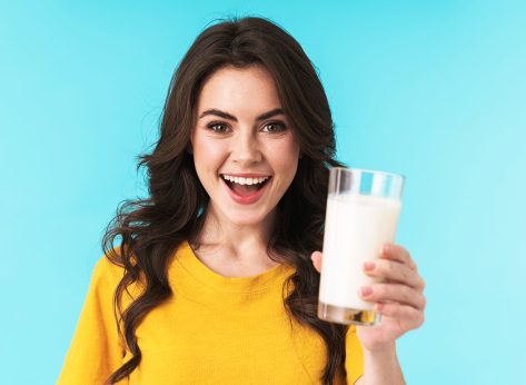 Image of happy positive optimistic young beautiful woman posing isolated over blue wall background holding milk.