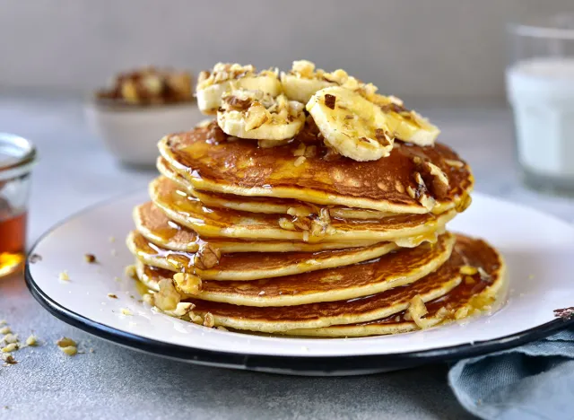 Homemade delicious banana pancakes with walnuts and maple syrup on a plate on a white slate, stone or concrete background.