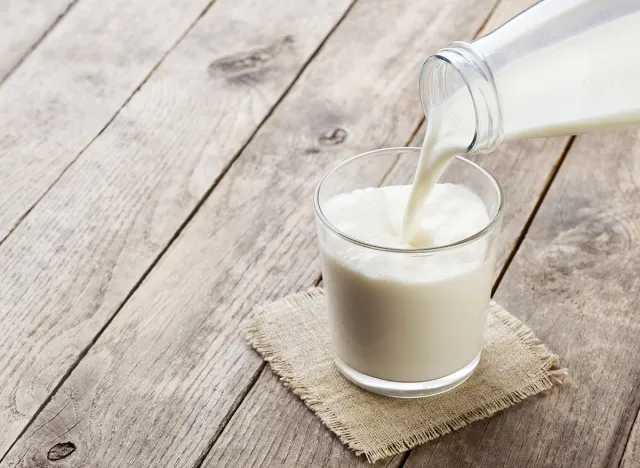 milk pouring from bottle into glass on old wooden table