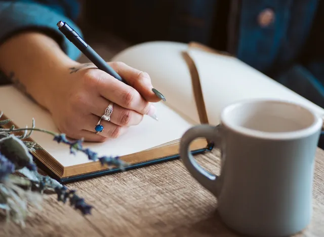 Hand writing in journal with coffee mug