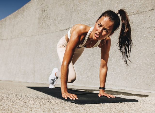 Healthy woman doing mountain climbers exercise. Female in sportswear exercising on a mat outdoors.