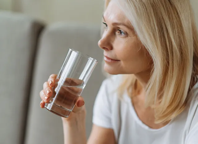 Follow healthy lifestyle. To be healthy. Mature beautiful caucasian woman holding a glass of clean water, taking care of her health, the daily norm of water