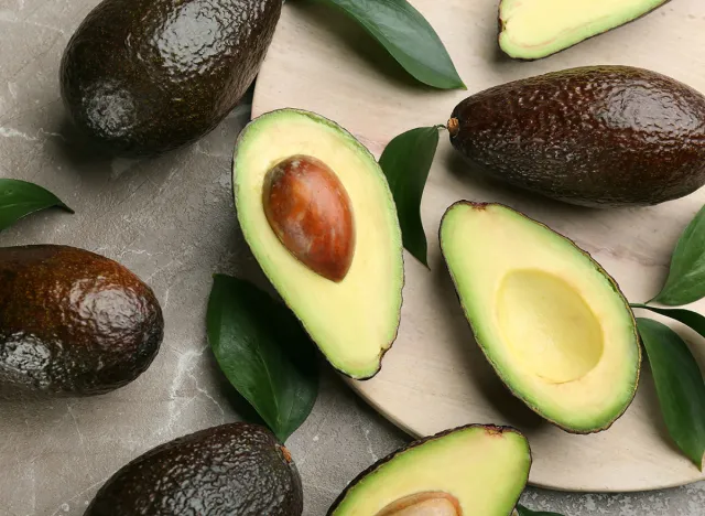 Whole and cut avocados on grey marble table, flat lay