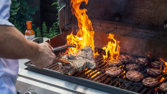 Man cooking marinated lamb joint and beef burgers on a garden barbecue