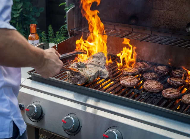 Man cooking marinated lamb joint and beef burgers on a garden barbecue