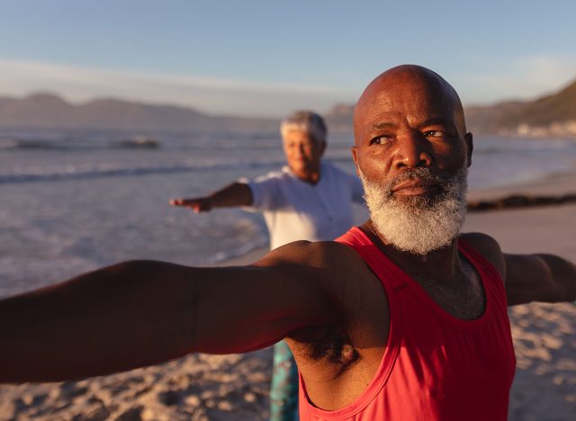 Senior african american couple performing stretching exercise together at the beach. fitness yoga and healthy lifestyle concept