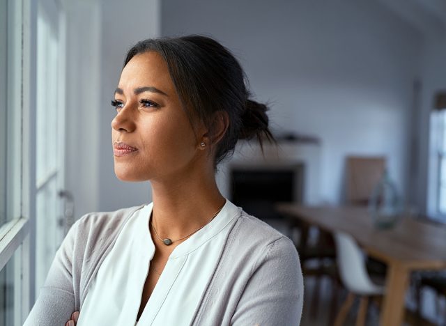 Mature african woman looking outside window with uncertainty. Thoughtful mid adult woman looking away through the window while thinking about her future business after pandemic. Doubtful lady at home.