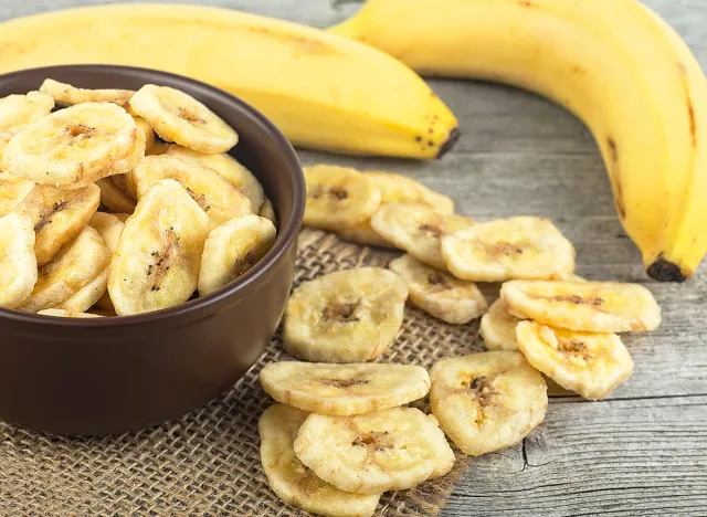 Healthy Food - Dried banana slices and fresh bananas on wooden table. Banana chips. Banana dessert.