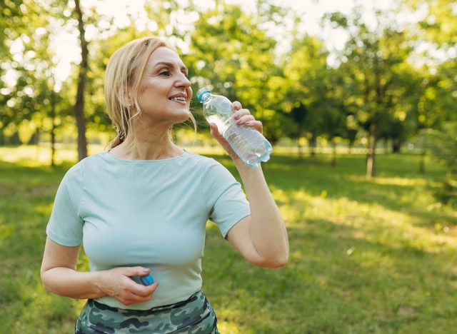 Mature woman drinks water while exercising in the park. The concept of a healthy lifestyle. Copy space