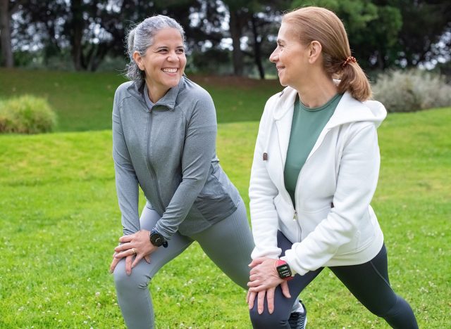 Cheerful senior friends exercising in park. Women in sportive clothes stretching on cloudy day. Sport, friendship concept