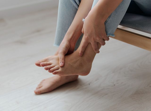 Closeup shot of pain leg foot suffering tanned beautiful young Asian woman touch ankle at home interior living room. Injuries Poor health Illness concept. Cool offer Banner