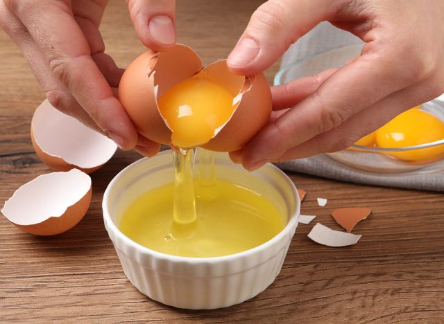 Woman separating egg yolk from white over bowl at wooden table, closeup