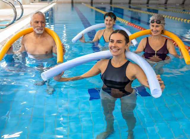 Group of people working with float noodles at water fitness class