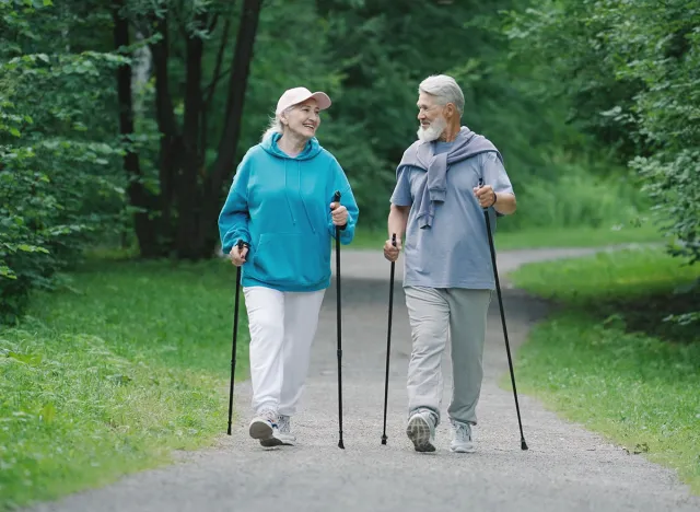 Elder family hikers pair fun stroll. Two happy old sportsman enjoy romantic date. Old sporty couple nordic walk poles green nature forest park. Elderly people fit workout. Old grandparents joy smile.