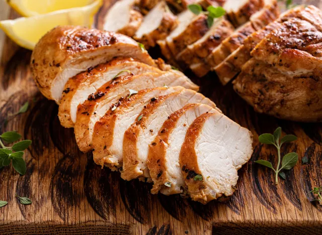 Grilled or roasted chicken breast, whole and sliced on a wooden serving plate