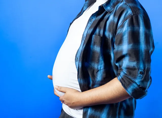 obesity, healthy food and weight loss concept. Side view of an Indian man touching and showing belly fat