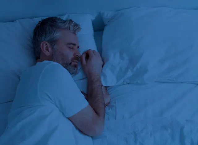 Top view of single handsome grey-haired middle aged man wearing pajamas peacefully sleeping alone in bed at night at home, empty pillow and free space next to him