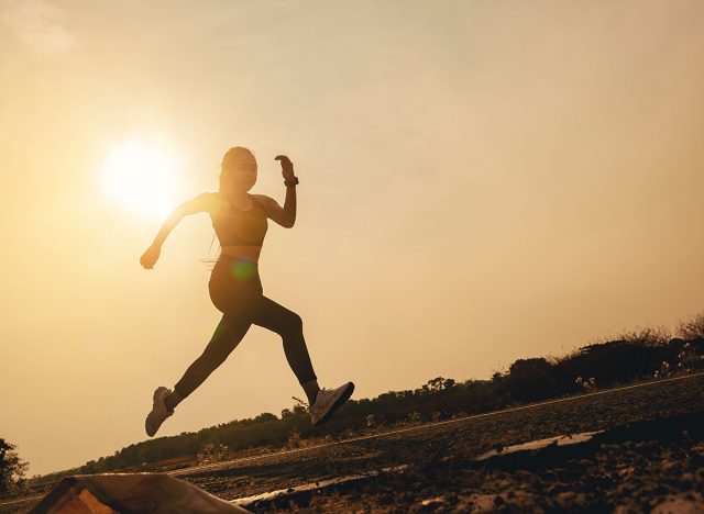 Silhouette of young woman running sprinting on road. Fit runner fitness runner during outdoor workout with sunset background.